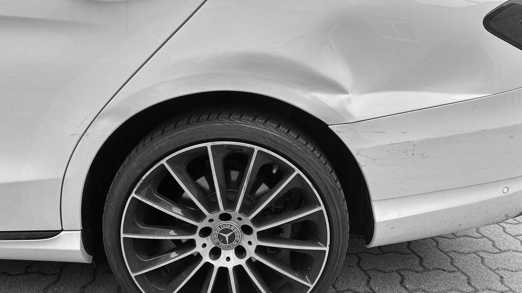 Schwarz-Weiß-Aufnahme der hinteren linken Seitenwand eines Mercedes C-Klasse T-Modell über dem Rad, eingedrückt bis zum Stoßfänger