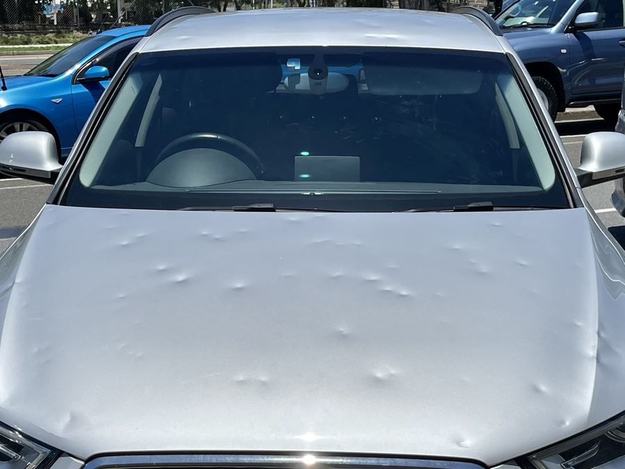 Silberner Audi Q3 von vorn, Motorhaube und Dach übersät mit Hageldellen, die sich im Licht als helle Mulden abzeichnen