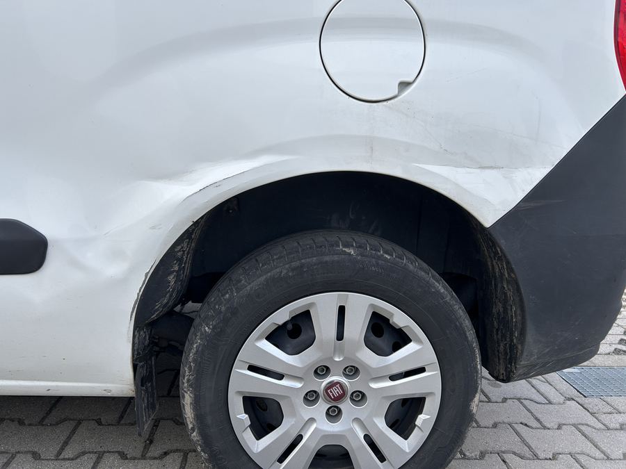 Hintere Seitenwand eines weißen Fiat Doblò: Über dem Radlauf zieht sich eine lange Delle durch das Blech, die Kante zum Radlauf ist eingedrückt
