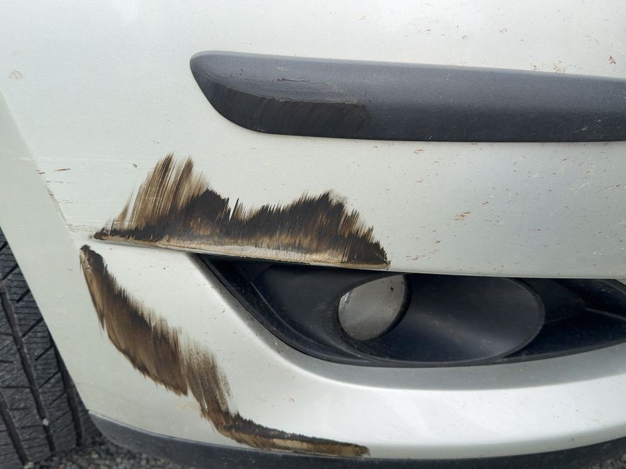 Schrammen mit braunem Farbübertrag am vorderen Stoßfänger eines silbernen Toyota Auris neben dem Nebelscheinwerfer, der typische Fall für eine Teillackierung des Stoßfängers