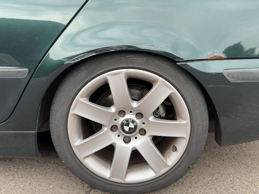 Hintere linke Seitenwand eines dunkelgrünen BMW 3er über dem Radlauf, eingedrückt, mit Schramme und aufgeplatztem Lack an der Kante, Reparaturkosten laut Gutachten 6.174 Euro brutto