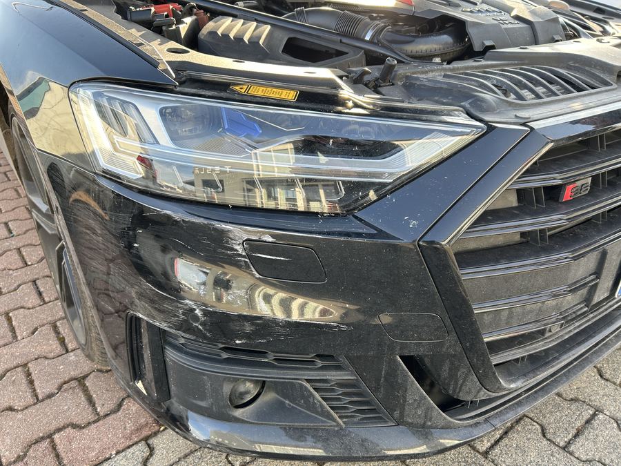 Front eines schwarzen Audi S8 mit geöffneter Motorhaube, Scheinwerfer und Stoßfänger rechts verschrammt, Reparaturkosten laut Gutachten 25.412 Euro brutto