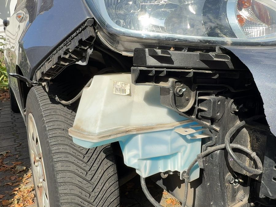 Vordere rechte Ecke eines grauen Hyundai i10 mit abgerissener Stoßfängerecke, freiliegendem Wischwasserbehälter und beschädigtem Scheinwerfer, Reparaturkosten laut Gutachten 6.620 Euro brutto