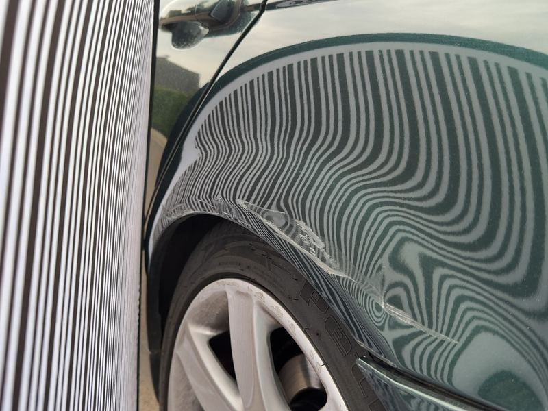 Hintere linke Seitenwand eines dunkelgrünen BMW 3er unter der Dellenleuchte, das Streifenmuster zeigt die Verformung, Reparaturkosten laut Gutachten 6.174 Euro brutto